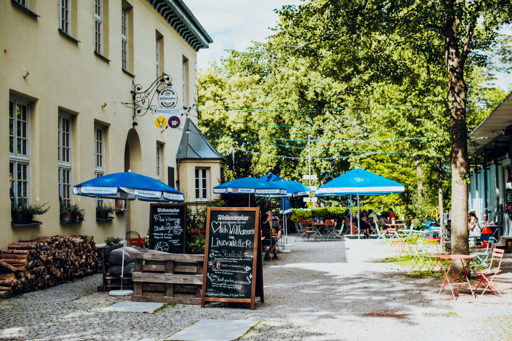 Der Stadtgarten Freising im Sommer: Essen und Trinken unter Sonnenschirmen und dem Schatten der Bäume.
